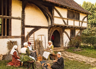 Tudor costumed women doing basketwork outside timber frame house